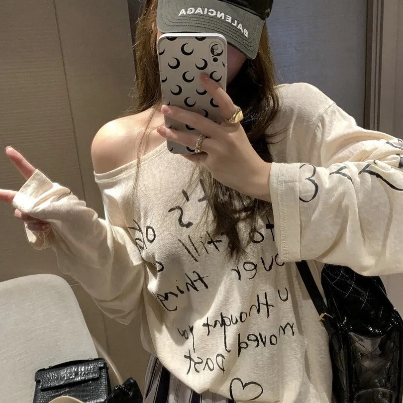 Kvinnors avslappnad oversized topp med avskuren axel design och konstnärlig text Mirla-Eva Jonsson
