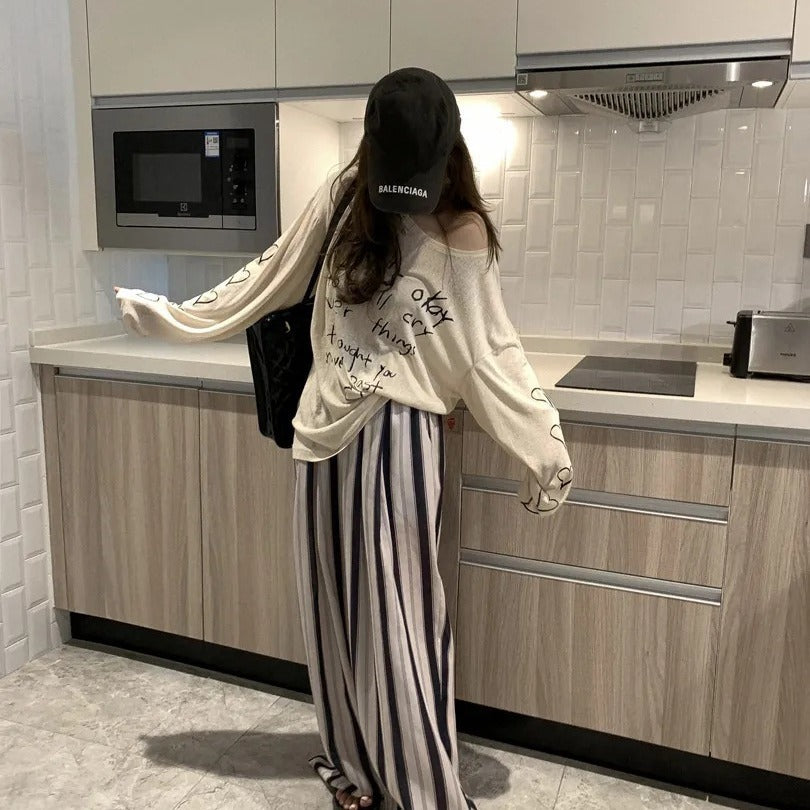 Kvinnors avslappnad oversized topp med avskuren axel design och konstnärlig text Mirla-Eva Jonsson