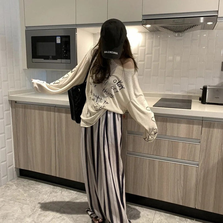Kvinnors avslappnad oversized topp med avskuren axel design och konstnärlig text Mirla-Eva Jonsson