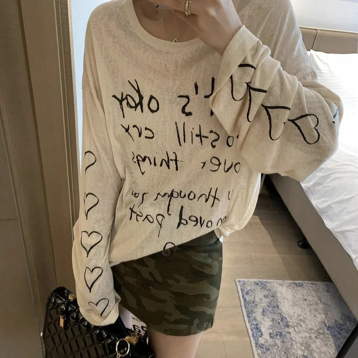 Kvinnors avslappnad oversized topp med avskuren axel design och konstnärlig text Mirla-Eva Jonsson