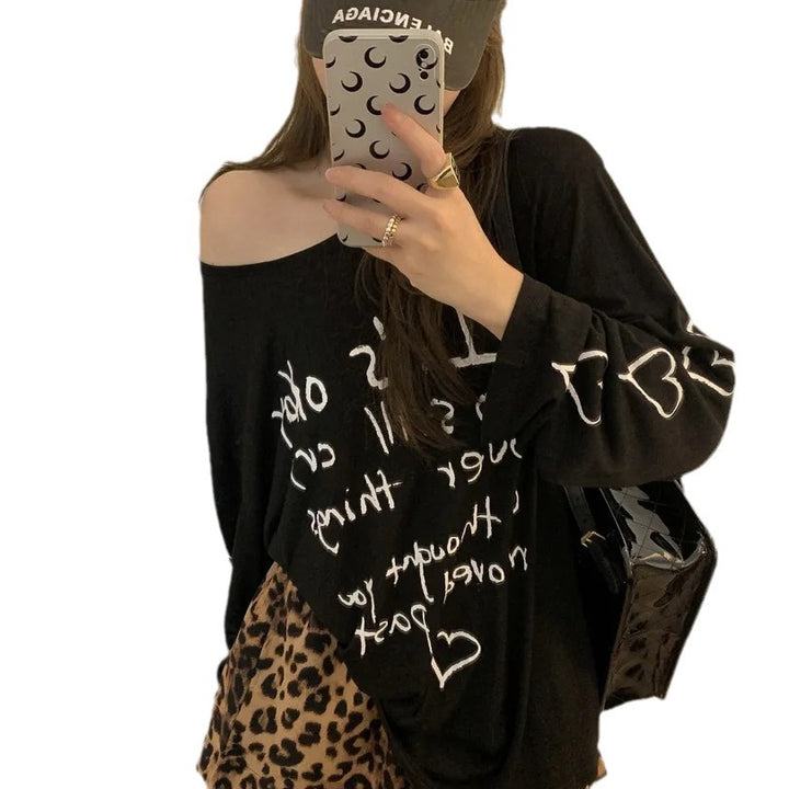 Kvinnors avslappnad oversized topp med avskuren axel design och konstnärlig text Mirla-Eva Jonsson