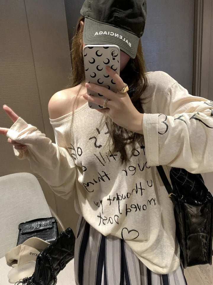 Kvinnors avslappnad oversized topp med avskuren axel design och konstnärlig text Mirla-Eva Jonsson